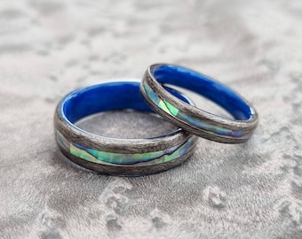May include: Two matching rings with a blue resin inlay and a grey wood grain pattern with iridescent abalone shell accents.