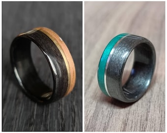 May include: Two black wood rings with contrasting inlays. One ring has a gold inlay and the other has a green and silver inlay.