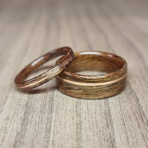 Könnte beinhalten: Zwei Holz-Eheringe mit einer dünnen Gold-Einlage. Die Ringe sind braun mit dunkelbraunen Streifen.