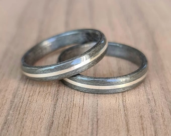 May include: Two black and silver wedding bands with a thin silver inlay. The bands are stacked on top of each other.