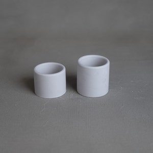 May include: Two white ceramic planters, one larger than the other, on a gray background.