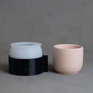 May include: A white silicone mold with a black plastic base and a light pink ceramic planter.