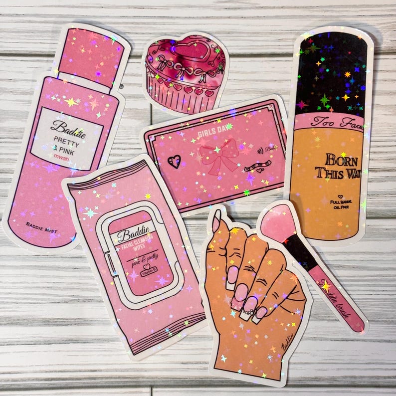 May include: A set of pink and gold holographic stickers featuring makeup and beauty products. The stickers include a bottle of pink mist, a package of facial cleansing wipes, a compact with a bow, a cupcake, a hand holding a makeup brush, and a bottle of foundation with the text "Too Faced Born This Way".