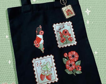 May include: Black tote bag featuring four decorative patches with floral and stamp designs. One patch is a map of Palestine with flowers, and others depict stamps with red flowers and strawberries. A keychain with a stamp design hangs from the handle.