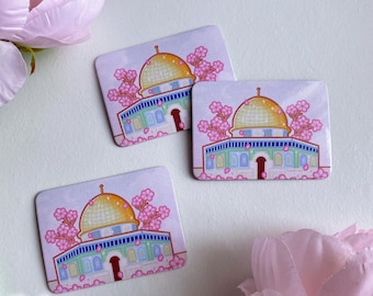 May include: Three rectangular stickers featuring a gold-domed building with a blue roof and pink cherry blossoms. The building has a red door and green and blue accents. The stickers are on a white surface with pink flowers.