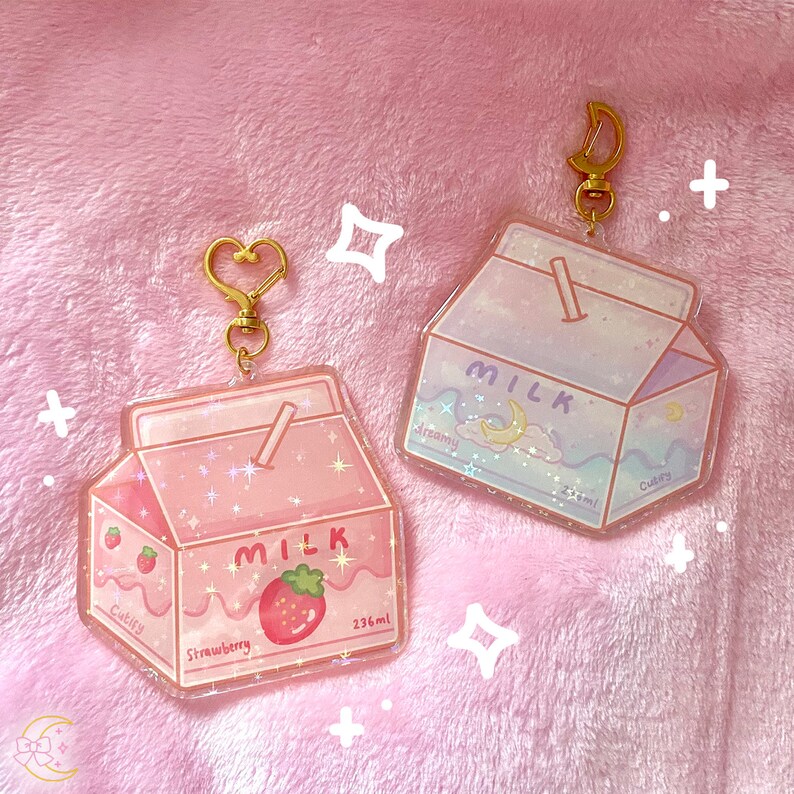 May include: Two acrylic milk carton keychains. One is pink with a strawberry design and the word "Strawberry". The other is blue with a dreamy moon and cloud design. Both have gold-colored clasps and the word "Milk". Each carton is 236ml.