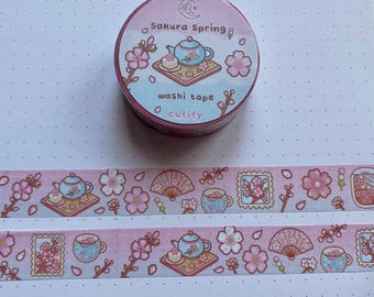 May include: A roll of pink and blue washi tape with a floral and tea set design. The tape features cherry blossoms, teacups, teapots, and fans. The tape is labeled "Sakura Spring" and "washi tape" with a small logo of a crescent moon and star.