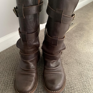 May include: A pair of brown leather knee-high boots with multiple buckles and straps.
