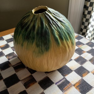 May include: A round ceramic vase with a textured surface. The vase is green and yellow with a mottled glaze.
