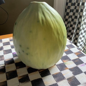 May include: A light green ceramic vase with a rounded, organic shape. The vase has a textured surface and a subtle green glaze.