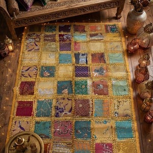 Peut inclure: Un tapis patchwork rectangulaire composé d'une grille de carrés de tissu multicolores dans des tons or, bleu sarcelle, violet, rouge et marron. Chaque carré présente des broderies, des paillettes et des fils métalliques uniques, bordés d'un cadre jaune.