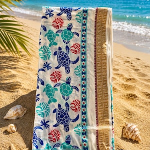 Op de afbeelding: Een rechthoekig, gebroken wit textiel met een herhalend patroon van blauwe en turquoise zeeschildpadden, afgewisseld met rode cirkelvormige koraalmotieven. De stof heeft een verticale bloemenrand en een brede gouden geometrische bies.