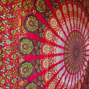 May include: A large fabric wall hanging featuring a vibrant red background with a central circular mandala pattern. The design includes intricate paisley motifs in yellow, green, and white, surrounded by a dense floral border on the left side.