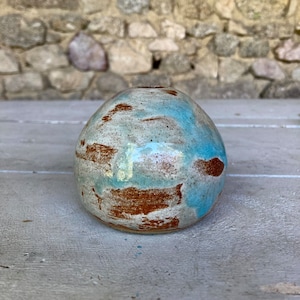 Könnte beinhalten: Eine kleine, runde Keramikvase mit einer blauen, weißen und braunen Glasur. Die Vase hat eine gesprenkelte Textur und eine leicht unebene Oberfläche.