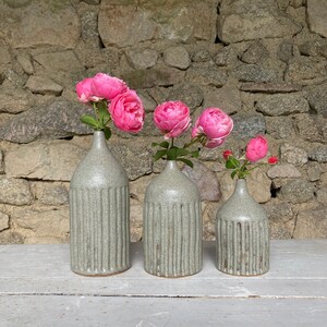 Könnte beinhalten: Drei graue Keramikvasen mit gerippter Textur, nach Größe geordnet, mit rosa Rosen in jeder Vase.