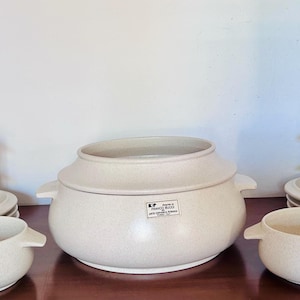 May include: A set of three ceramic mugs with a speckled, cream-colored glaze. Each mug features a different hand-painted floral design in shades of blue, green, and yellow. The mugs have a simple, rounded shape.