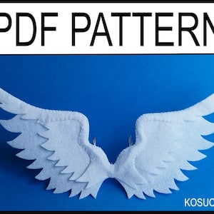 May include: White felt angel wings with a layered design, set against a blue background. The text "PDF PATTERN" is at the top, and the name "KOSUCAS" is at the bottom. The wings are designed for crafting.