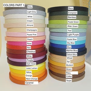 May include: Stacks of colorful craft ribbon spools in various shades, including grey, black, green, blue, yellow, orange, and brown. The image includes a color chart with names like "Grey," "Black," and "Caramel." The text reads "COLORS PART 1."