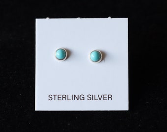 May include: A pair of sterling silver stud earrings with round, light blue turquoise stones. The earrings are displayed on a white card with the text "STERLING SILVER" printed in black.