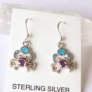 May include: Sterling silver crab earrings with purple and blue gemstone accents. The crab design features a central purple stone and blue accents, with the text "STERLING SILVER" on the display card.
