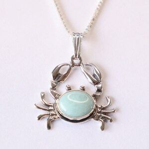 May include: A silver crab pendant necklace with a light blue gemstone. The crab is detailed with claws and legs.