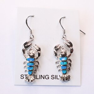 May include: Sterling silver earrings featuring a blue opal scorpion design. The earrings are on a white card with the text "Sterling Silver".