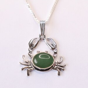 May include: A silver crab pendant necklace with a green gemstone. The crab is detailed with claws and legs.