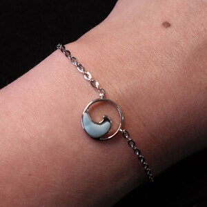 May include: A silver chain bracelet with a small, round charm featuring a white wave design.