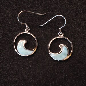 May include: A pair of silver earrings with a blue and white wave design. The earrings are circular and have a dangling hook.