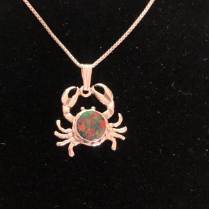 May include: A silver crab pendant necklace featuring a green, red and black opal gemstone. The necklace has a fine chain.