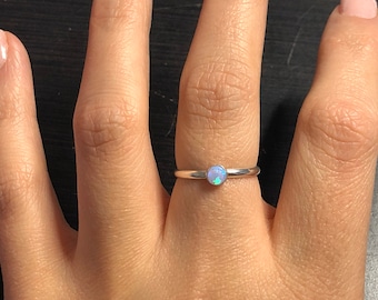May include: A silver ring with a small, round, iridescent opal gemstone.