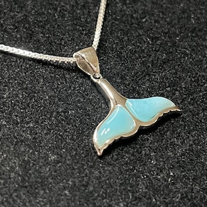 May include: A silver necklace with a blue whale tail pendant. The pendant is made of silver and has a blue enamel finish.