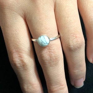May include: A silver ring with a white marble stone.