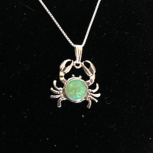 May include: A silver crab pendant necklace with a green opal stone in the center. The necklace has a silver chain.