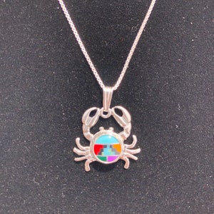 May include: A silver necklace with a crab pendant. The crab is made of silver and has a blue, red, green, yellow, and purple inlay.