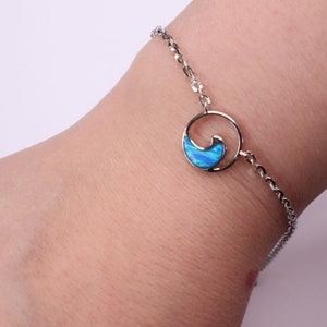 May include: A silver chain bracelet with a blue opal wave charm. The charm is in a circle with a silver outline.
