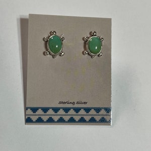 May include: A pair of sterling silver earrings with green turquoise stones. The earrings are oval shaped and have a decorative border.