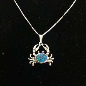 May include: A silver necklace with a crab pendant featuring a blue and green opal stone.