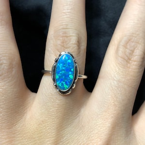 May include: A silver ring with a blue oval opal gemstone set in a silver bezel. The ring is on a person's finger.