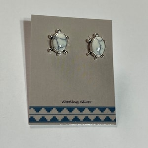 May include: A pair of sterling silver earrings with white howlite stones. The earrings are oval shaped and have a decorative design around the stones.