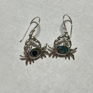 May include: A pair of silver dangle earrings featuring a crab design with an iridescent abalone shell inlay.