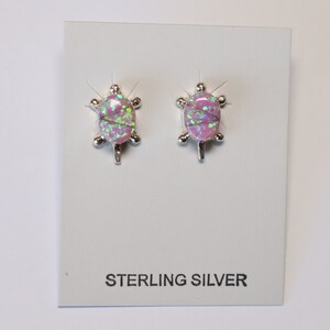 May include: A pair of sterling silver turtle stud earrings. Each earring features a pink and green oval-shaped stone set in a silver turtle design. The earrings are displayed on a white card with the text "STERLING SILVER".