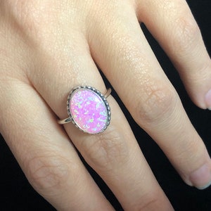 May include: A silver ring with a pink oval opal gemstone set in a beaded bezel.