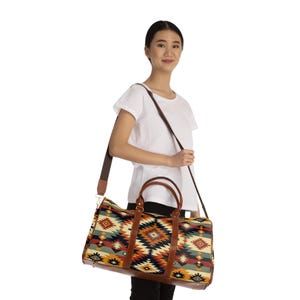 May include: A colorful duffel bag with a geometric pattern in shades of red, orange, blue, and cream. The bag has brown leather handles and a shoulder strap. The bag is being carried over the shoulder.