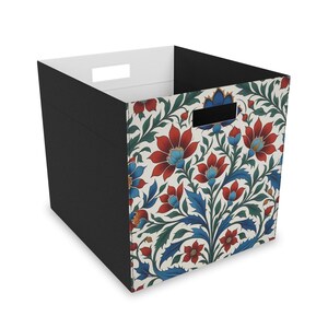 May include: A black fabric storage cube with a floral pattern featuring red, blue, and green flowers on a white background. The cube has a cut-out handle on the top.