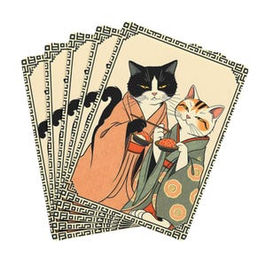 May include: A stack of playing cards featuring a stylized illustration of two cats in traditional Japanese attire. One cat is black and white, the other is orange and white. The cats are holding food. The cards have a decorative border.