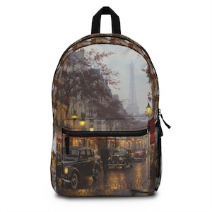 May include: A backpack featuring a printed scene of a Parisian street at dusk with vintage cars on a cobblestone road, glowing street lamps, and the Eiffel Tower in the distance. The bag has a black top handle, black zippers, and side mesh pockets.