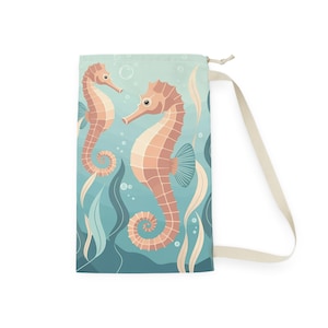 May include: A drawstring bag featuring a whimsical underwater scene. Two seahorses in shades of peach and cream are set against a teal background with aquatic plants and bubbles. The bag has a cream-colored strap and a drawstring closure.
