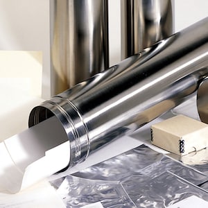 May include: A cylindrical stainless steel storage tube with a matching removable cap, containing a rolled white paper document. Beside the tube are several flat white paper sheets, a small square cardboard box, and multiple silver foil pouches.