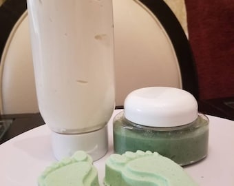 May include: A white lotion bottle and a small jar with a white lid, both on a white plate. Two light green foot-shaped soaps are in front of the jar. The lotion bottle is tall and cylindrical.